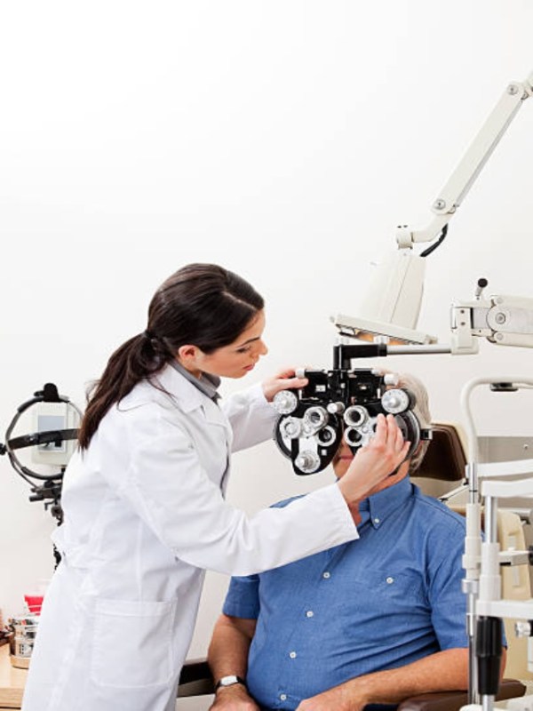 Female optometrist performing eye checkup with phoropter at clini