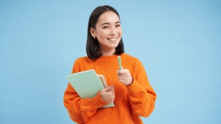 Education and students. Happy asian woman, holding notebooks and laughing, smiling at camera, enjoys going to University or College, blue background.