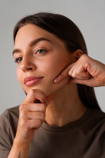 Portrait of young lady pressing fingers on puffy cheeks in tank top and looking funny front view