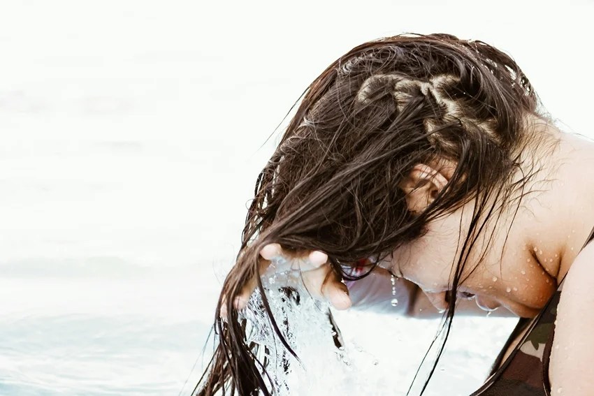 Woman washing hair with hot water affecting hair health and shine.