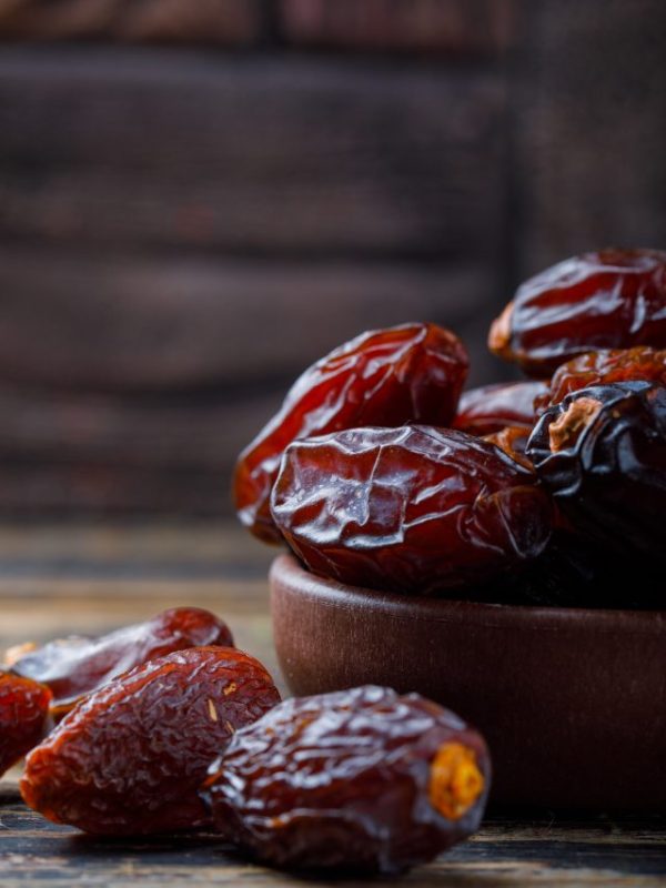 Sweet dates in a clay plate on stone tile and wooden background, close-up.